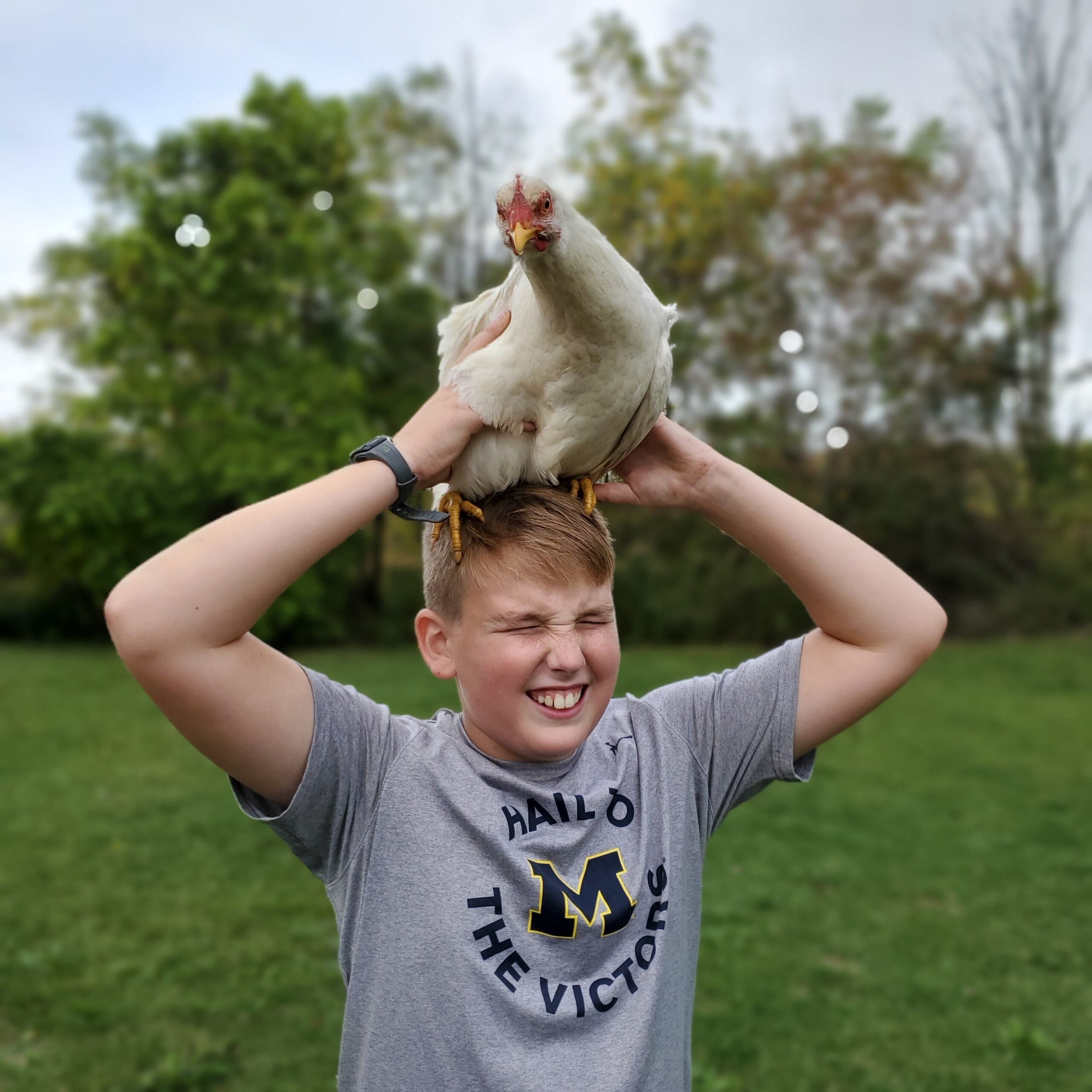 happy kid holding a chicken on top of his head